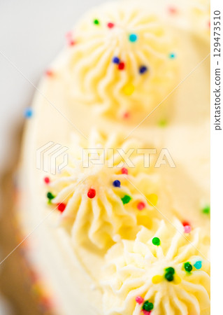 Top view showing symmetrical buttercream swirls arranged in a circle on a white frosted cake. Each swirl is adorned with multicolored sprinkles. The image is brightly lit with a clean and minimal 129473510