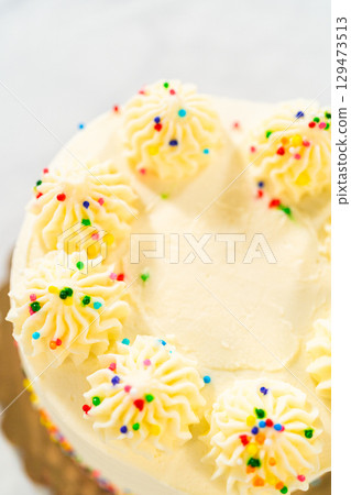 An overhead close-up image of a white cake topped with uniform piped dollops of vanilla frosting. Each frosting swirl is decorated with multi-colored nonpareils. The cake is centered in the frame An overhead close-up image of a white cake topped with uniform piped dollops of vanilla frosting. Each frosting swirl is decorated with multi-colored nonpareils. The cake is centered in the frame 129473513