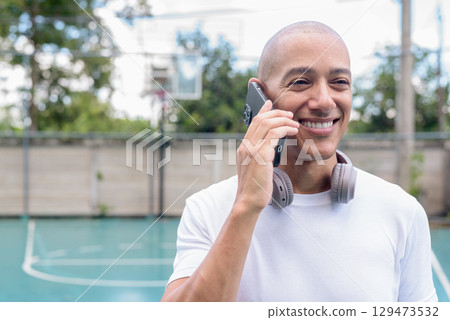 Latin man using smartphone on outdoor basketball court, urban sports fitness lifestyle 129473532