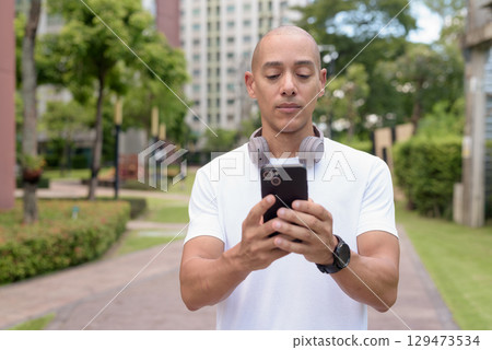 Latin bald man using phone while walking in city, digital lifestyle and active wellness concept Latin bald man using phone while walking in city, digital lifestyle and active wellness concept 129473534