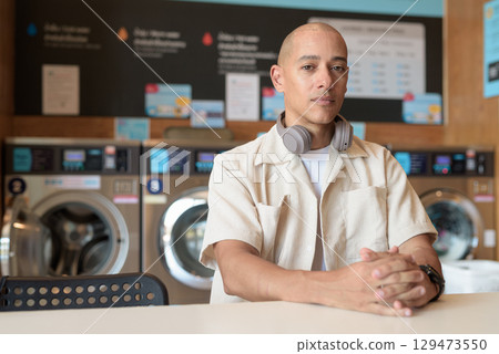 Bald Latin man sitting in laundromat with washing machines in background Bald Latin man sitting in laundromat with washing machines in background 129473550