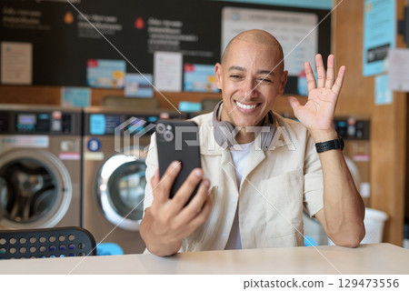 Bald Latin man using smartphone in laundromat with washing machines in background Bald Latin man using smartphone in laundromat with washing machines in background 129473556