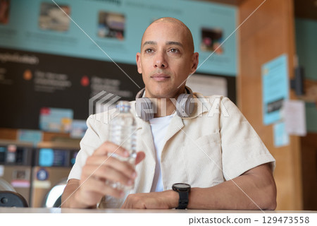 Bald Latin man drinking water in laundromat with washing machines behind Bald Latin man drinking water in laundromat with washing machines behind 129473558