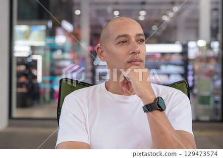 Bald Latino man sitting outdoors in coffee shop, confident summer portrait and wellness lifestyle 129473574