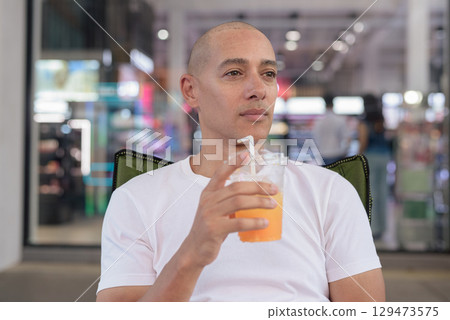 Bald Latino man sitting and drinking orange juice in coffee shop restaurant during summer 129473575