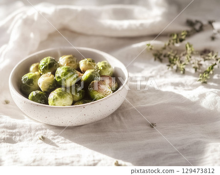A clean and minimal presentation of steamed Brussels sprouts served in a round white ceramic bowl on a soft tablecloth. Great for healthy eating and vegetarian meals. 129473812