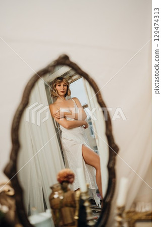 in the mirror of a beautiful young woman with blonde hair in a white dress 129474313