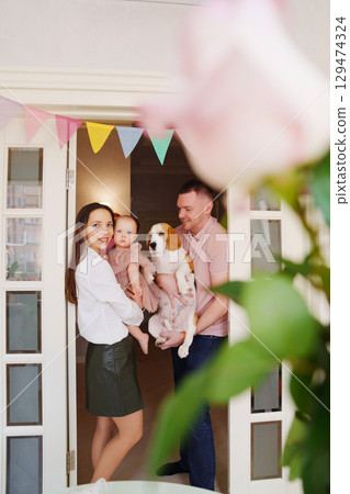 parents hold baby daughter in the doorway with a garland of colorful flags.  129474324