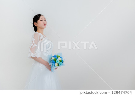 Beautiful bride with bouquet against white wall Beautiful bride with bouquet against white wall 129474764