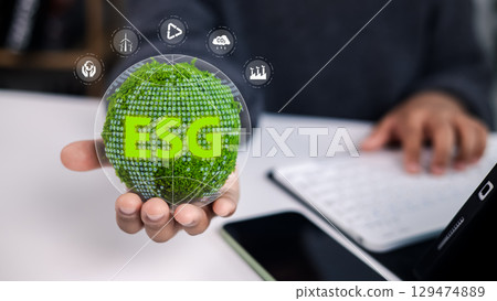 Hand holding a green globe with ESG text, surrounded by icons for wind energy, tree planting, CO2 reduction, and business growth, symbolizing sustainability and corporate social responsibility. 129474889