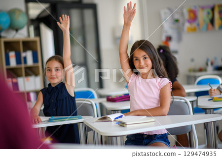 School children sitting at the desk in classroom on the lesson, raising hands. School children sitting at the desk in classroom on the lesson, raising hands. 129474935