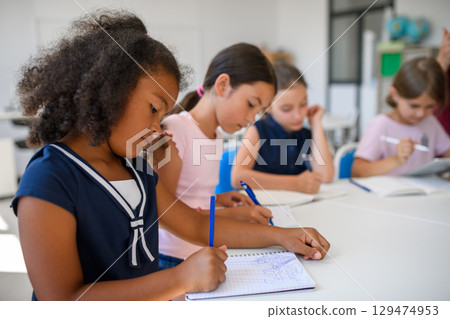 Schoolkids sitting at the desk in classroom, taking notes. 129474953