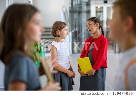 Happy schoolkids talking in school hallway. 129474956