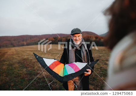 Senior couple flying a kite during warm autumn evening. Senior couple flying a kite during warm autumn evening. 129475063