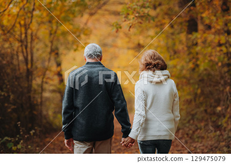 Elderly couple walking hand in hand through autumn forest 129475079