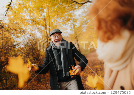 Senior man and woman enjoying a walk in fall, throwing fallen leaves. Senior man and woman enjoying a walk in fall, throwing fallen leaves. 129475085