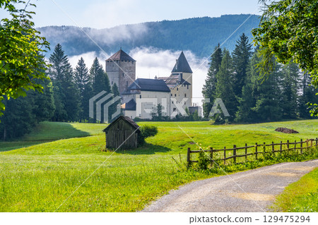 Mauterndorf Castle rises majestically amid lush green fields and towering trees. The misty backdrop adds a magical touch, inviting visitors to explore its rich history and stunning architecture. 129475294