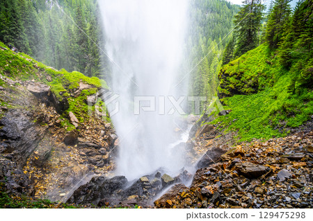 Johannes Waterfall cascades dramatically among lush green forests in Obertauern, Austria. Misting water creates a refreshing atmosphere, making it a serene spot for nature lovers and hikers. 129475298