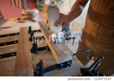 Joiner man hands gluing wooden beams before clamping forming solid board. Surface smooth, even coat 129475397