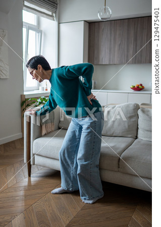 Senior woman gripping lower back in severe pain from spinal attack. Slipped disc, arthritic spasm Senior woman gripping lower back in severe pain from spinal attack. Slipped disc, arthritic spasm 129475401
