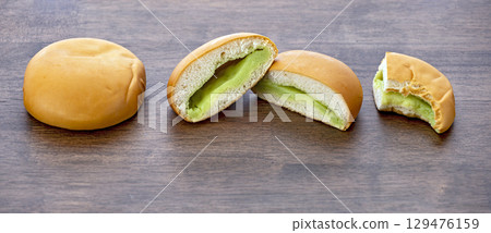 Three stages of pandanus custard bread on a wooden plate one whole, one cut in half, and one partially eaten, showing its soft texture and sweet filling. Three stages of pandanus custard bread on a wooden plate one whole, one cut in half, and one partially eaten, showing its soft texture and sweet filling. 129476159