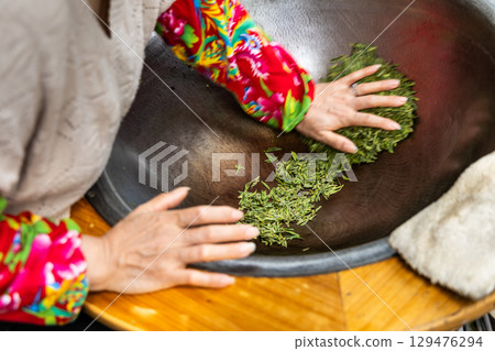 Working pressing the longjing tea leaves in a pan to flatten the leaves as second step in pan-fry process Working pressing the longjing tea leaves in a pan to flatten the leaves as second step in pan-fry process 129476294