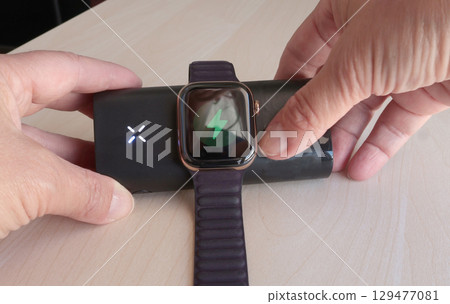 Woman charges her smart watch using portable wireless charger in room. Modern lifestyle, mobile technology, travel. Woman charges her smart watch using portable wireless charger in room. Modern lifestyle, mobile technology, travel. 129477081