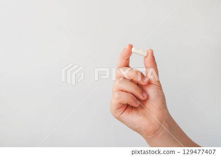 a child hand holding a white capsule pill against a plain background 129477407