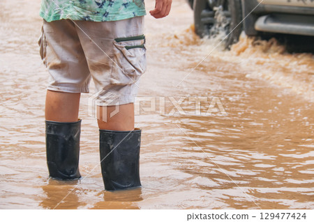 Black rubber boots walking through floodwater 129477424