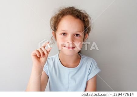 child girl in a light blue shirt holds up a white capsule between her fingers against a plain background 129477614