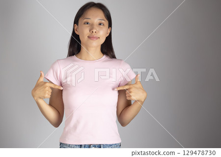 Young girl wearing a light pink t-shirt and jeans, is pointing to her chest with both hands 129478730