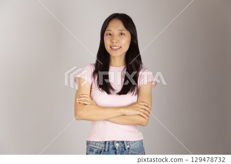 Young woman is standing with her arms crossed, smiling slightly, and looking directly at the camera. 129478732