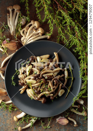 Fried shimeji mushrooms with thyme and garlic on a black plate. Fried shimeji mushrooms with thyme and garlic on a black plate. 129479007