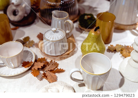Autumn table setting with white cups and yellow oak leaves on the table Autumn table setting with white cups and yellow oak leaves on the table 129479023