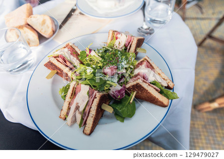 white plate with sliced chicken sandwiches and green salad in a restaurant 129479027