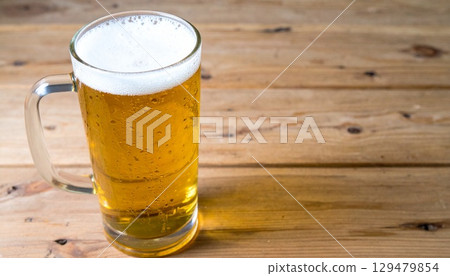 木桌上一杯帶有白色泡沫的金色拉格啤酒的特寫鏡頭 129479854