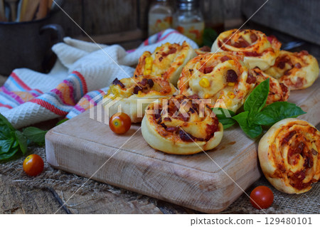 Small pizza with mozzarella cheese, ham, basil, cherry tomatoes. Buns of yeast dough on wooden background. Mini pizzas. Homemade baking. Small pizza with mozzarella cheese, ham, basil, cherry tomatoes. Buns of yeast dough on wooden background. Mini pizzas. Homemade baking. 129480101