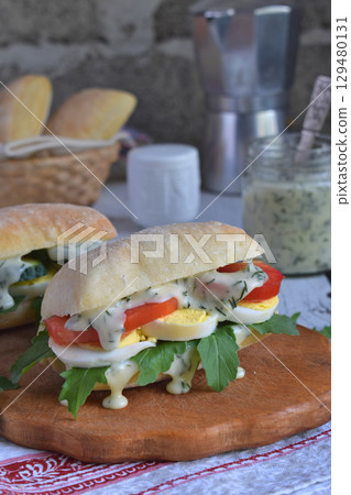 Sandwich from bun panini, cheese sauce, eggs, arugula, tomato and cucumber. Breakfast or snack. Vegetarian food. Healthy diet concept. Rustic photo. Copy space 129480131