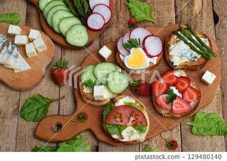 Set of healthy whole wheat bread sandwiches with fuits, vegetables, cheese and leafy green herbs on picnic wooden table. Ciabatta sandwich bar or buffet. Top view. Making lunch time snacks concept 129480140