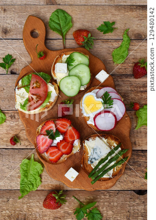Set of healthy whole wheat bread sandwiches with fuits, vegetables, cheese and leafy green herbs on picnic wooden table. Ciabatta sandwich bar. Top view. Lunch time snacks concept. Vegetarian food 129480142