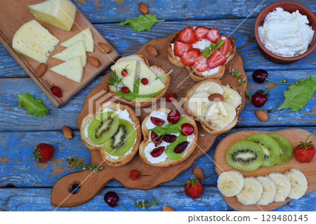 Set of assorted healthy wholewheat bread sandwiches with fruit, cheese and leafy green herbs on picnic wooden table. Ciabatta sandwich bar or buffet. Top view. Making lunch time snacks concept. 129480145