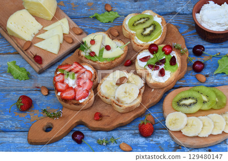 Set of assorted healthy wholewheat bread sandwiches with fruit, cheese and leafy green herbs on picnic wooden table. Ciabatta sandwich bar or buffet. Top view. Making lunch time snacks concept. Set of assorted healthy wholewheat bread sandwiches with fruit, cheese and leafy green herbs on picnic wooden table. Ciabatta sandwich bar or buffet. Top view. Making lunch time snacks concept. 129480147