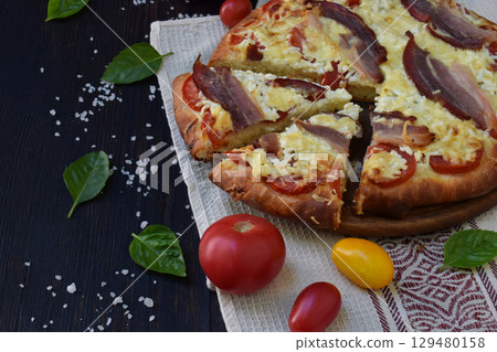 Homemade delicious pizza with cheese, tomato and prosciutto ham on a dark wooden background. 129480158