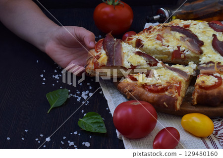Homemade delicious pizza with cheese, tomato and prosciutto ham on a dark wooden background. 129480160