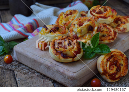 Small pizza with mozzarella cheese, ham, basil, cherry tomatoes. Buns of yeast dough on wooden background. Mini pizzas. Homemade baking. 129480167