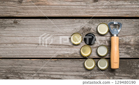 Aerial view of beer caps and bottle openers lined up on a rustic wooden table 129480190