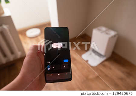 Freelancer working while robot vacuum cleans the floor controlled via smartphone app for convenience 129480675