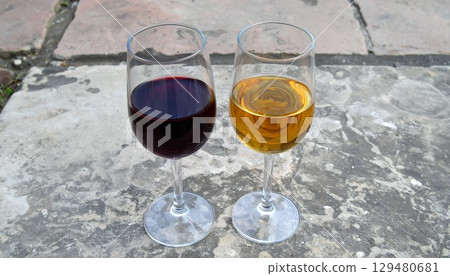 Close-up of two wine glasses of different colors placed on textured stone 129480681