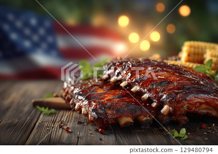 Juicy barbecue ribs coated in rich sauce sit on a rustic wooden table. Behind, a vibrant American flag adds a touch of patriotism, perfect for summer barbecues or festive occasions. 129480794