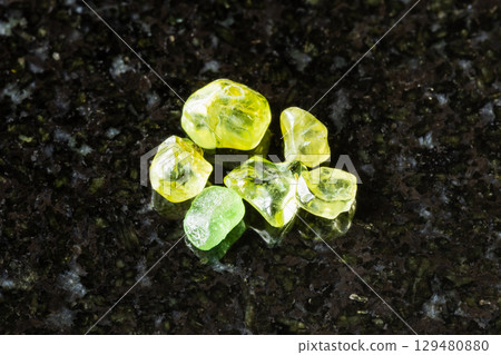 sample of raw peridot gemstones on black granite 129480880